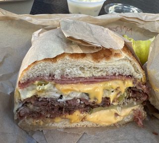 A sandwich with pastrami cheese and pickles on dutch crunch